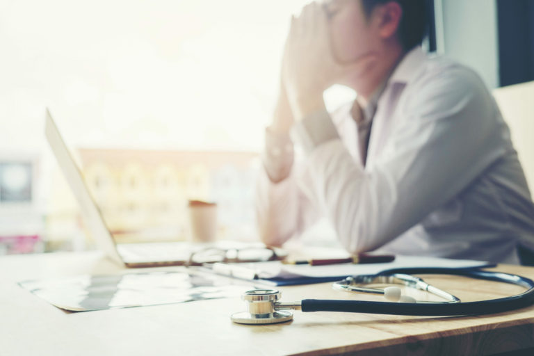 doctor at laptop with head in hands from physician burnout