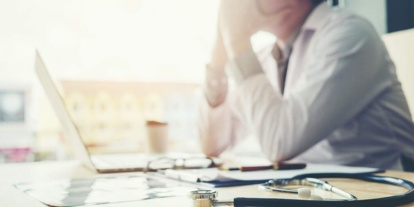 doctor at laptop with head in hands from physician burnout