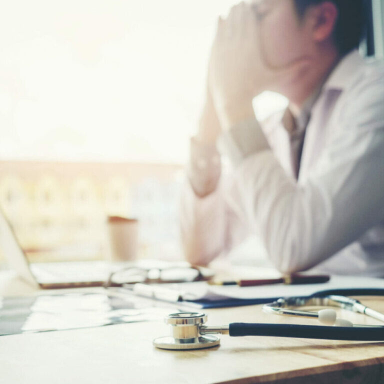 doctor at laptop with head in hands from physician burnout