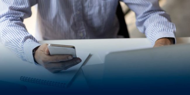 Processional holding cell phone and on laptop siting at a desk