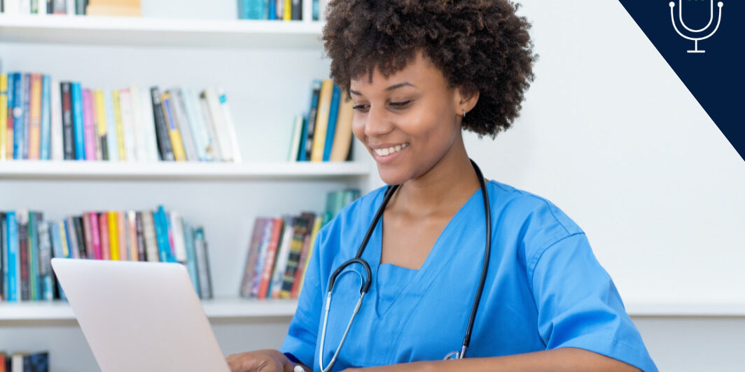 young nurse wearing scrubs and stethoscope studying at laptop with bookshelf behind her.