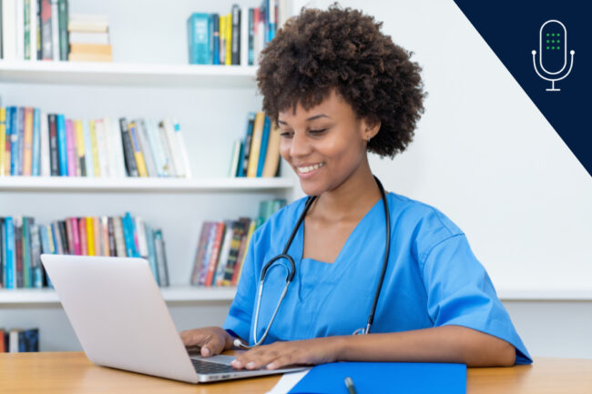 young nurse wearing scrubs and stethoscope studying at laptop with bookshelf behind her.