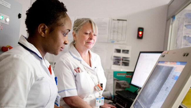 Two nurses working on a computer screen and x-ray monitor