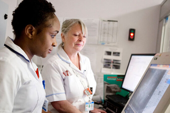 Two nurses working on a computer screen and x-ray monitor