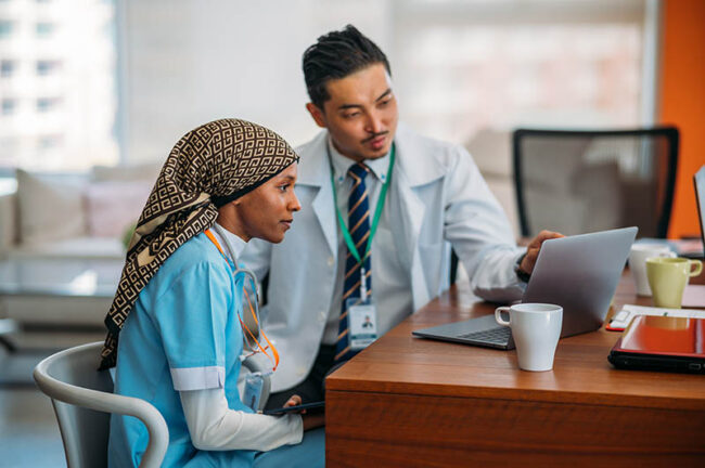 Doctor helping new nurse work through Epic onboarding on laptop