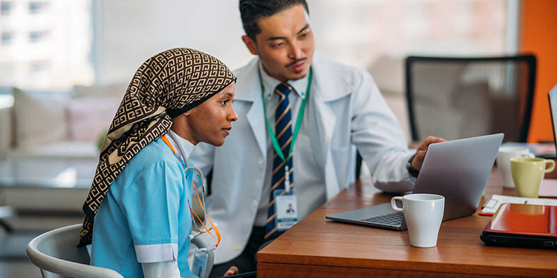 Doctor helping new nurse work through Epic onboarding on laptop