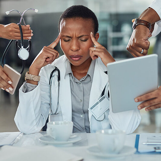 A stressed doctor presses her fingers to her temples, due to health worker burnout.