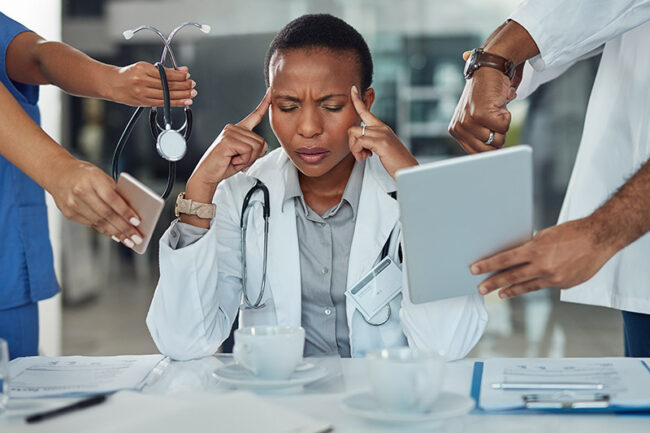 A stressed doctor presses her fingers to her temples, due to health worker burnout.