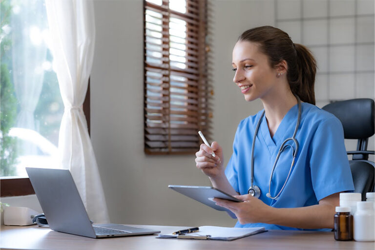 Female doctor focuses on laptop while she holds a tablet and stylus.