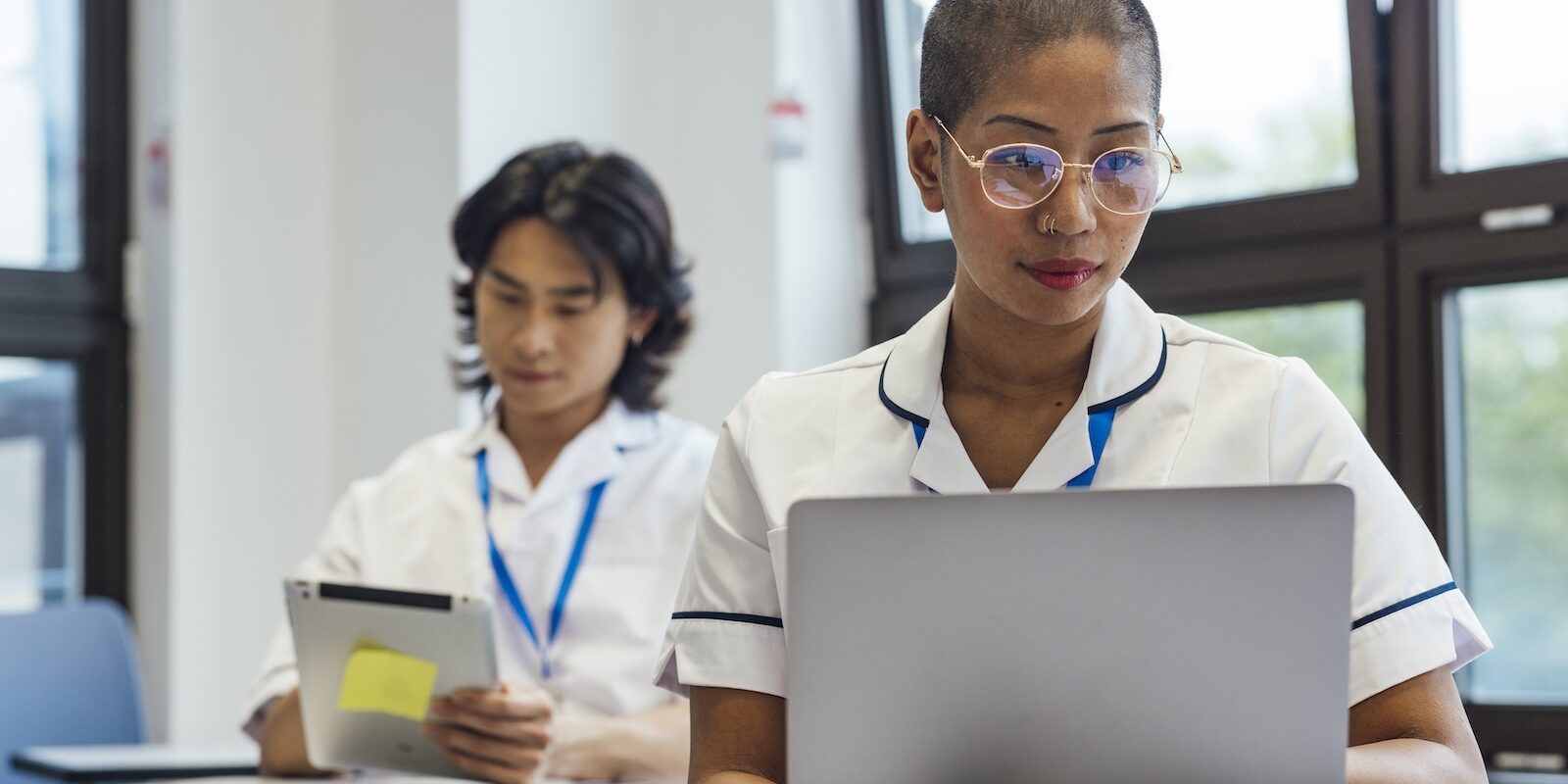 digital-adoption-platform-nhs-nurse-epr-learning Nurse using a laptop during a digital learning session, with a colleague reviewing a tablet in the background.